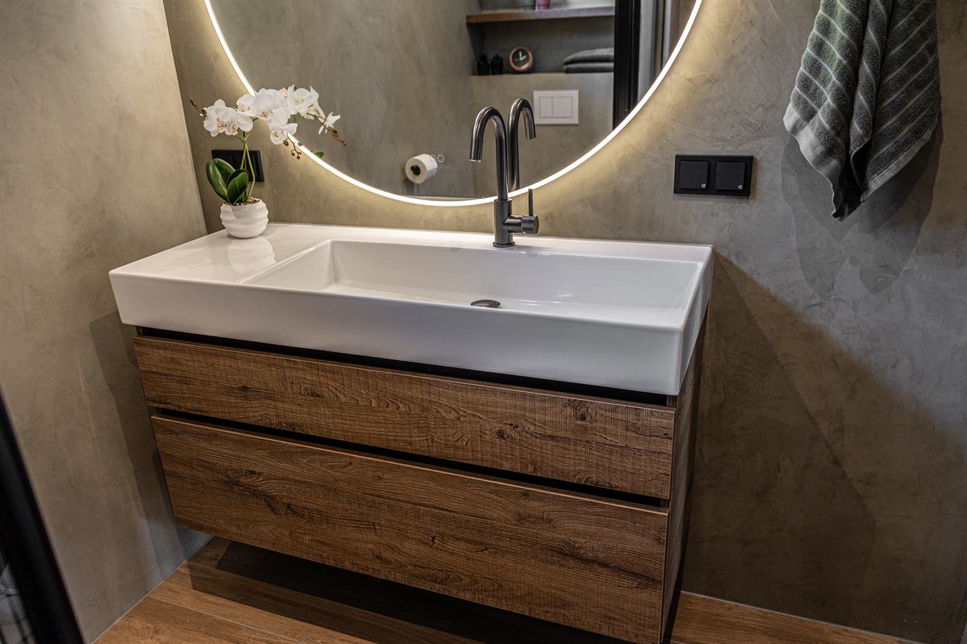 Badkamer met beton ciré wand, houten wastafelmeubel en matzwarte kraan